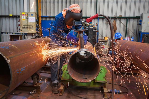 La molatura del lavoratore maschio usa scintille elettriche del tubo della molatura della mola all'interno della costruzione industriale.