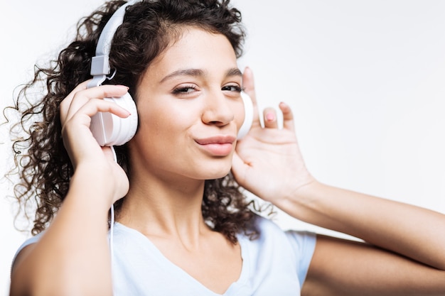 La musica porta gioia. Bella giovane donna dai capelli ricci che ascolta la musica in cuffia su wihte