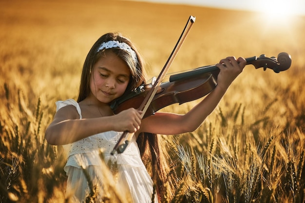 La natura ha musica per chi ascolta Inquadratura di una bambina carina che suona il violino in piedi in un campo di grano