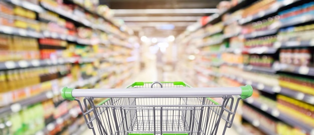 La navata laterale degli scaffali del supermercato con il carrello della spesa vuoto ha sfocato lo sfondo della luce del bokeh sfocato interno