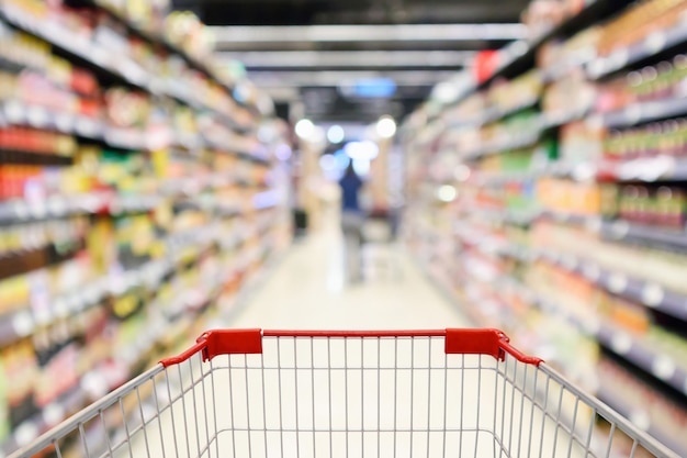 La navata laterale degli scaffali del supermercato con il carrello della spesa vuoto ha sfocato lo sfondo della luce del bokeh sfocato interno