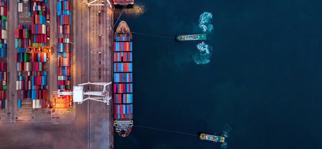 La nave portacontainer da carico con rimorchiatore sta lavorando la nave portacontainer fuori dal porto marittimo del terminal internazionale