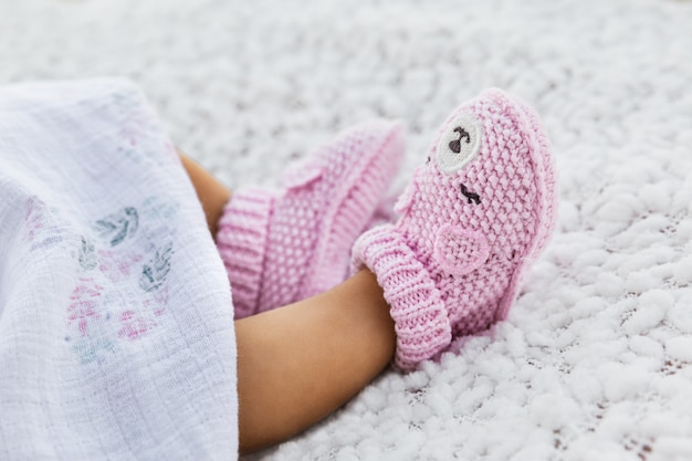 La neonata che indossa l'uncinetto tricottato contro una coperta bianca, scarpe rosa infantili