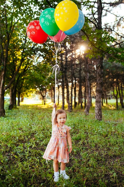 La neonata di 2-3 anni che tiene i palloni all'aperto. Festa di compleanno. Infanzia. Felicità.