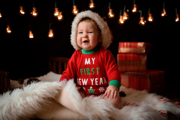 La neonata in un costume rosso di natale con le retro ghirlande si siede su una pelliccia