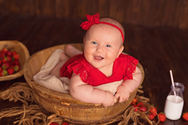 La neonata sorridente felice in un vestito rosso si trova sul suo stomaco e mangia le fragole e beve il latte