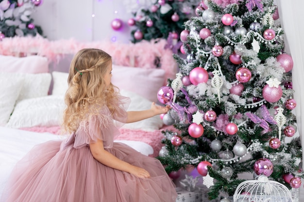 La neonata veste l'albero di Natale con un bellissimo vestito rosa, il nuovo anno e il concetto di Natale