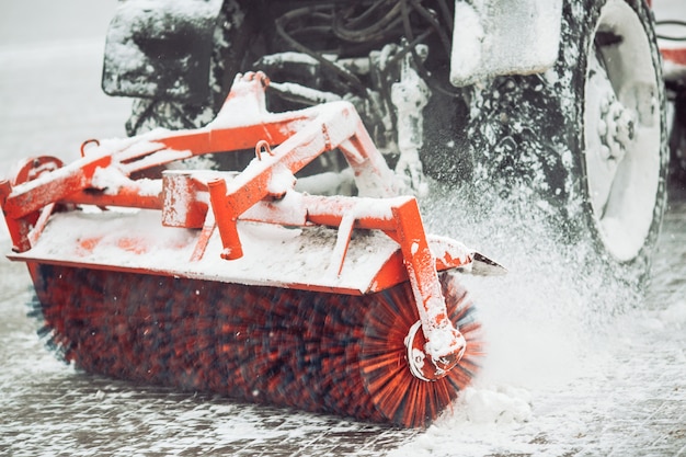 La neve di pulizia di servizio della città, un piccolo trattore con una spazzola girante cancella una strada nel parco della città dalla neve caduta fresca il giorno di inverno, spazzola - primo piano.