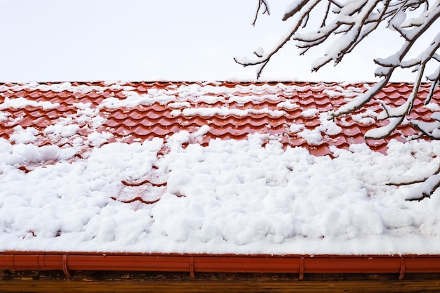 La neve rotola giù da un tetto di tegole metalliche dopo una forte nevicata in inverno Pericolo di caduta di neve dai tetti