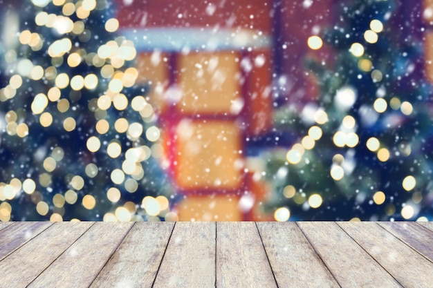 La neve sul fondo di festa di Natale con il piano d'appoggio di legno vuoto sopra la luce festiva del bokeh decora sull'albero di Natale. Per creare la visualizzazione del prodotto di montaggio