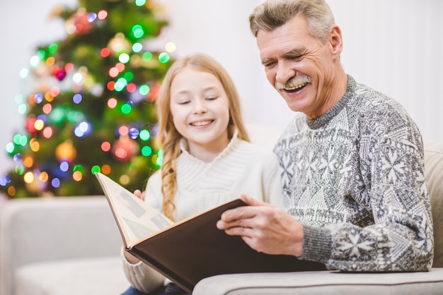 La nipote e il nonno guardano un album di foto vicino all'albero di Natale