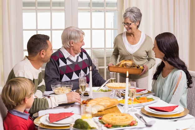 La nonna che tiene arrosto di tacchino con la famiglia al tavolo da pranzo