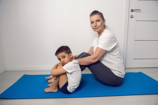 La nonna e il nipote sono seduti su un tappetino da yoga in un appartamento bianco