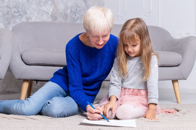 La nonna e la nipote dipingono insieme al pavimento del salotto. La donna adulta aiuta la ragazza a disegnare un'immagine