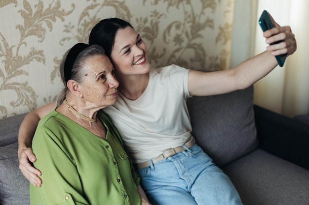 La nonna e la nipote guardano lo smartphone mentre si siedono sul divano Facendo un selfie al telefono