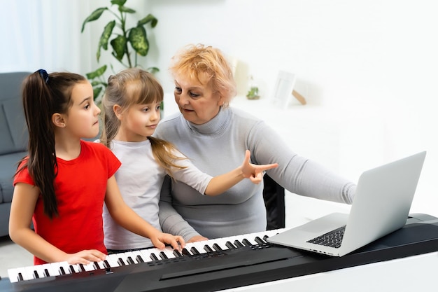 la nonna e le nipoti imparano a suonare il sintetizzatore per pianoforte su un laptop online a casa.