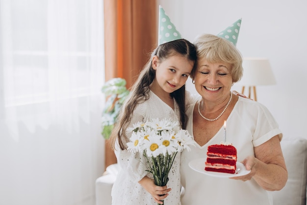 La nonna felice e sorridente riceve gli auguri di compleanno dalla nipote, la bambina e la signora anziana soffiano la candela sulla torta e festeggiano insieme il compleanno.