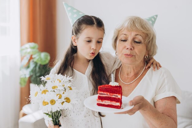La nonna felice e sorridente riceve gli auguri di compleanno dalla nipote, la bambina e la signora anziana soffiano la candela sulla torta e festeggiano insieme il compleanno.