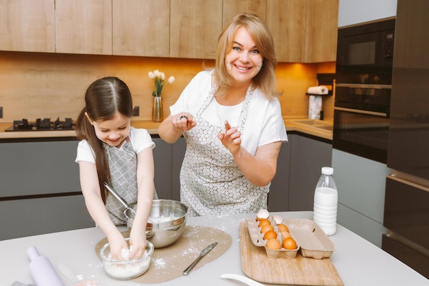 La nonna premurosa e la nipotina si divertono a cuocere i biscotti insieme nella cucina di casa Una nonna e una nipote anziane amorevoli preparano una deliziosa torta dolce