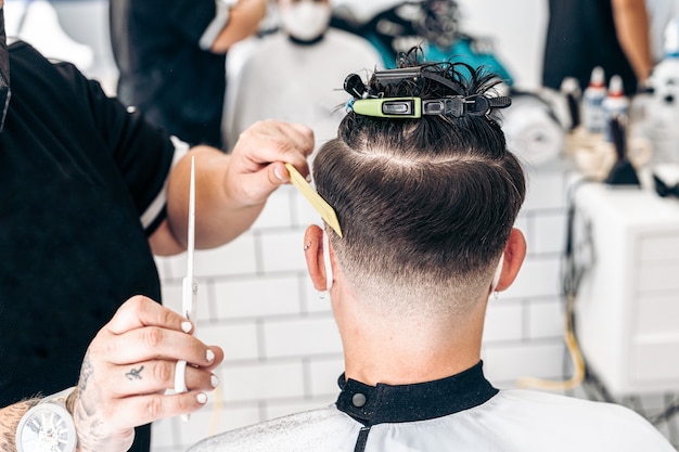 La nuca di un giovane uomo caucasico seduto in un parrucchiere mentre si fa tagliare i capelli.