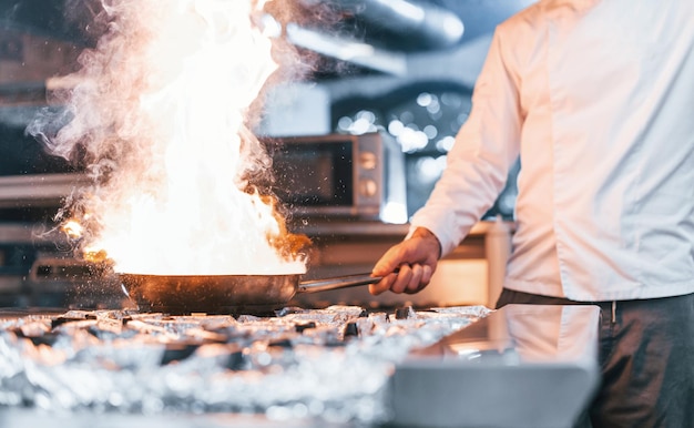 La padella è in fiamme Chef in uniforme bianca che cucina il cibo in cucina Giornata intensa di lavoro