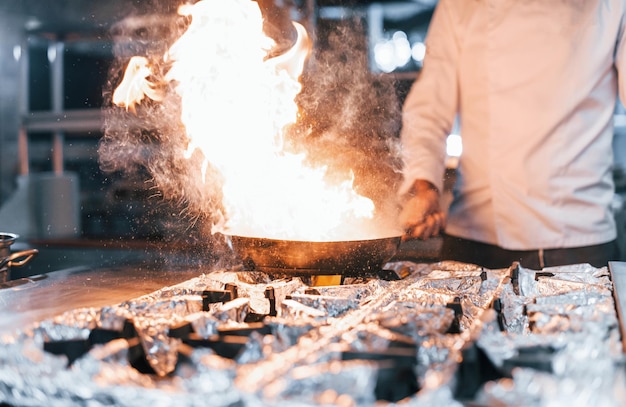 La padella è in fiamme Chef in uniforme bianca che cucina il cibo in cucina Giornata intensa di lavoro