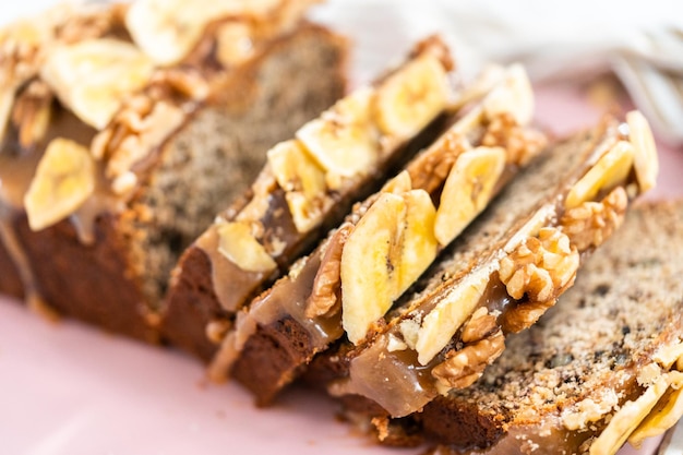 La pagnotta a fette di pane alle noci di banana ha spruzzato caramello fatto in casa su un tagliere rosa.