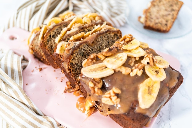 La pagnotta a fette di pane alle noci di banana ha spruzzato caramello fatto in casa su un tagliere rosa.