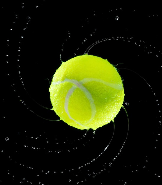 La palla da tennis colpisce l'acqua e schizza in aria Verda La pallina da tennis vola nella pioggia e schizza Spin schizza nelle gocce d'acqua Sfondio nero azione di congelamento isolata