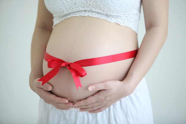 La pancia della donna di gravidanza con il nastro rosso e la mano della madre tengono con fondo bianco