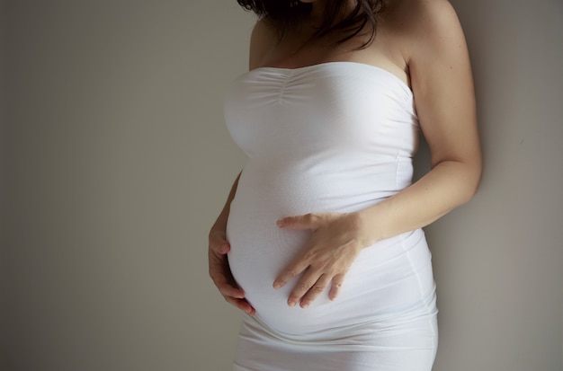 La pancia incinta dei dettagli della giovane donna in vestito bianco