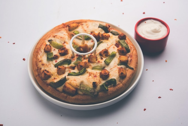 La Paneer Pizza è una versione indiana del piatto italiano condita con ricotta, servita in un piatto con salsa bianca. messa a fuoco selettiva