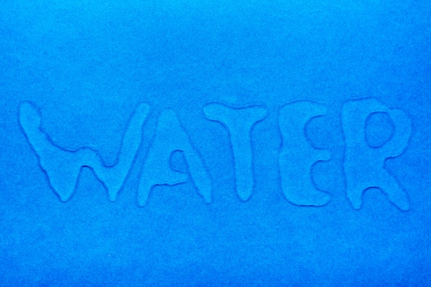 La parola "acqua" è scritta con gocce d'acqua su una superficie liscia blu.
