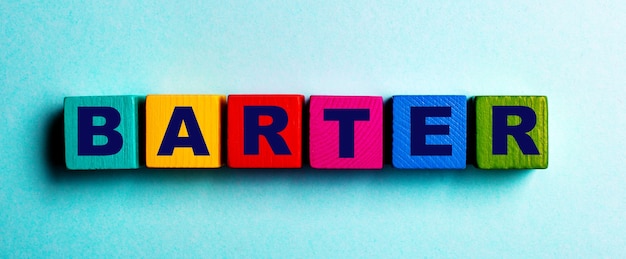 La parola BARATTO è scritta su cubi di legno luminosi multicolori su una superficie azzurra.