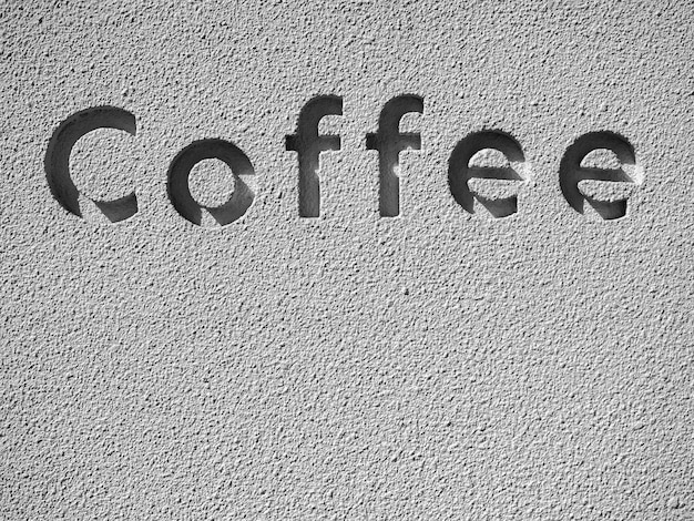 La parola caffè le lettere scolpite nelle parole sul muro di cemento grunge con copia spazio verticale Luce e ombra nel carattere intagliato sulla trama del muro di pietra di cemento grigio