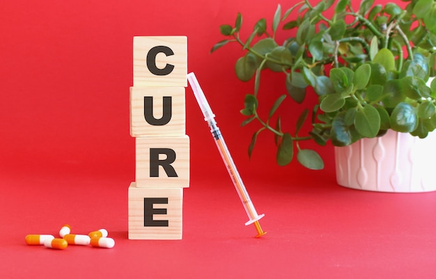 La parola CURE è composta da cubi di legno su un tavolo rosso con farmaci. Concetto medico.