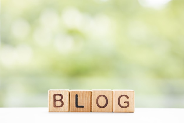 La parola del blog è scritta su cubi di legno su uno sfondo verde estivo Primo piano di elementi in legno