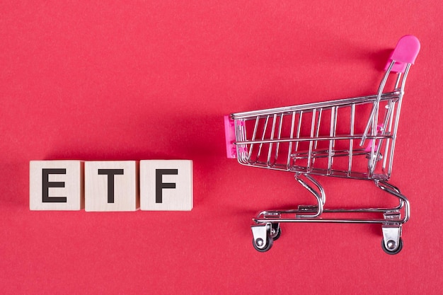 La parola ETF Exchange Trade Fund su cubi di legno su sfondo rosa con un carrello della spesa