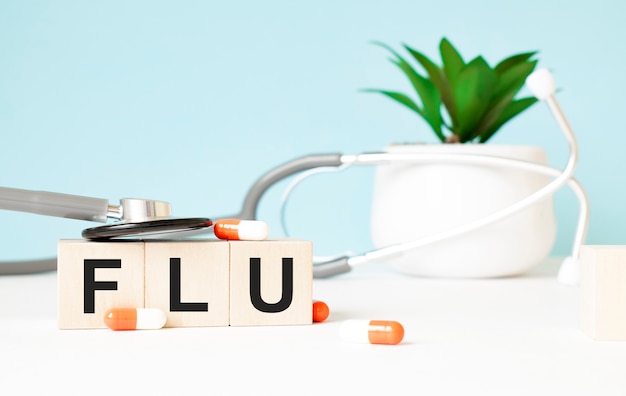 La parola FLU è scritta su cubi di legno vicino a uno stetoscopio su uno sfondo di legno. Concetto medico