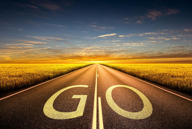 La parola GO scritta sulla strada dell'autostrada nel mezzo della strada asfaltata vuota al tramonto dell'ora d'oro Concetto per il successo