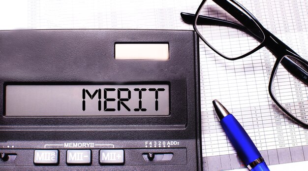 La parola MERITO è scritta nella calcolatrice vicino a occhiali con montatura nera e una penna blu