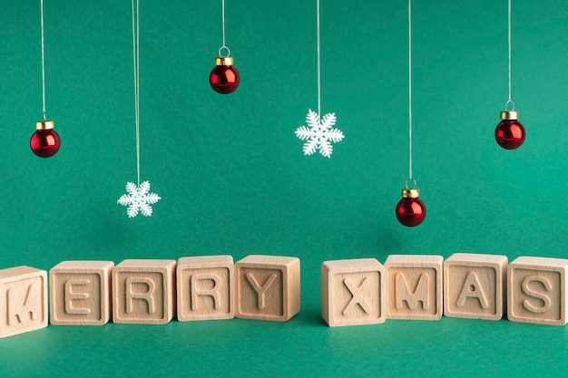 La parola Merry xmas composta da cubi di legno su sfondo verde Fiocchi di neve e palle di Natale Cartolina di Natale