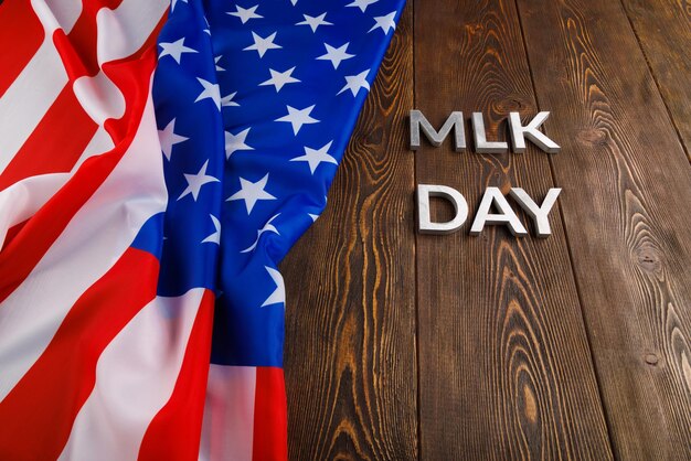 La parola MLK day posata con lettere di metallo argentato su una superficie di legno con bandiera USA stropicciata