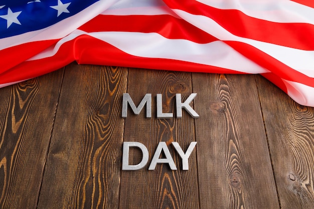La parola MLK day posata con lettere in metallo argentato su una superficie di legno con bandiera USA stropicciata sul lato superiore