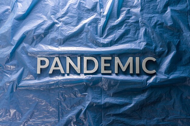 La parola pandemia posata con lettere d'argento su uno sfondo di pellicola di plastica blu stropicciata in una composizione piatta al centro