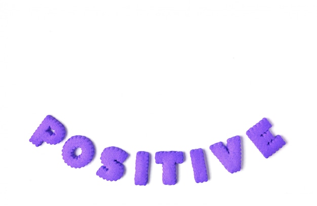 La parola POSITIVO scritto con i biscotti a forma di alfabeto di colore viola su bianco