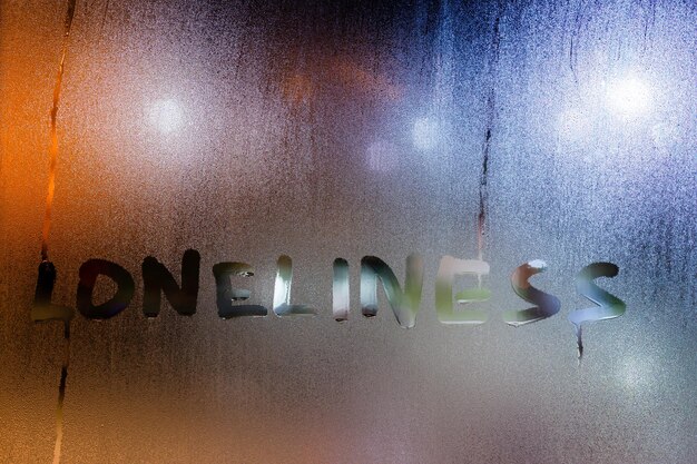 La parola solitudine scritta dal dito sul vetro bagnato notturno con luci sfocate sullo sfondo