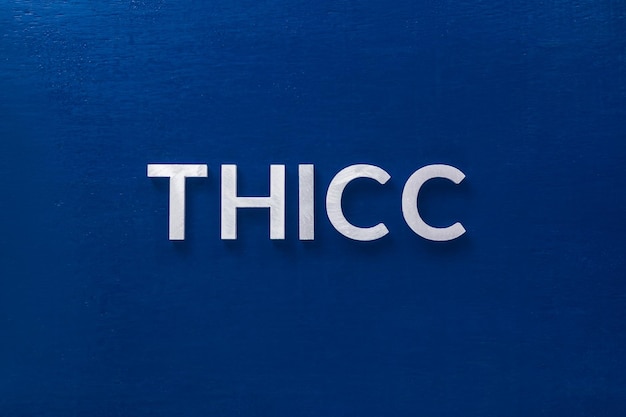 La parola thicc posata con lettere in metallo argentato su classica tavola blu in piatto con composizione centrale