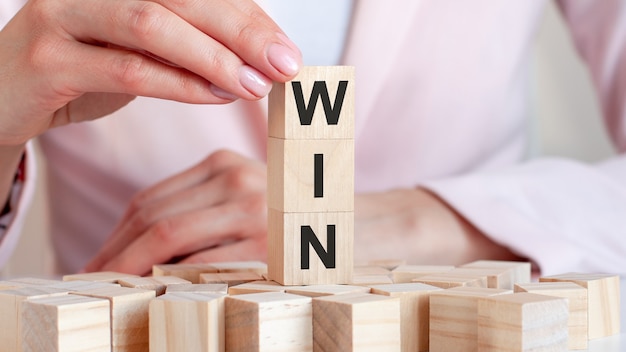 La parola Win su un giocattolo di legno blocca con le mani della donna, concetto di affari.