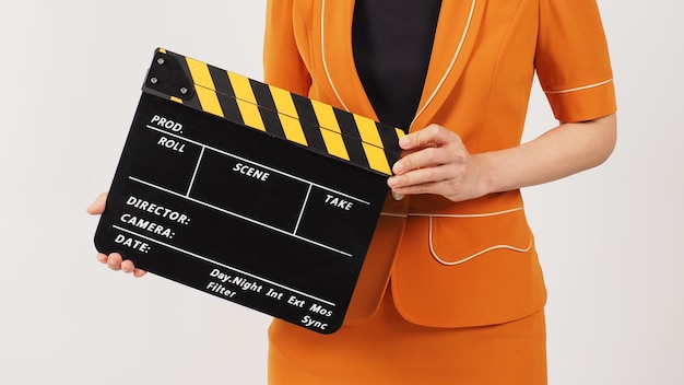 La parte del corpo della donna tiene un Clapperboard nero e giallo e indossa un abito giallo senape su sfondo bianco